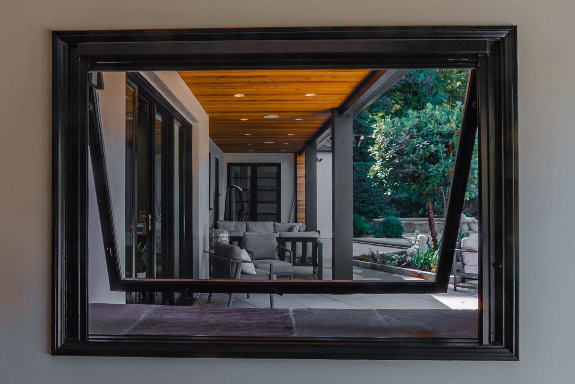 Framed view of a covered patio with chairs, wood ceiling, and greenery outside