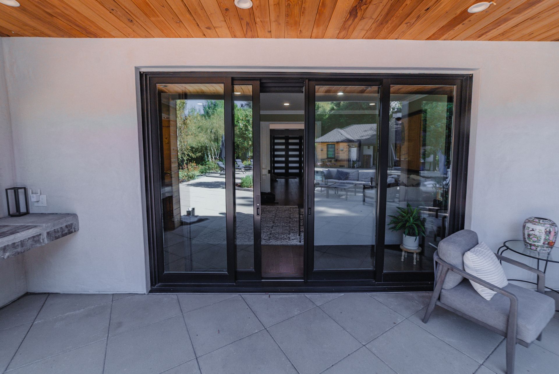Sliding glass doors open onto a patio with seating. Wooden ceiling and white walls.