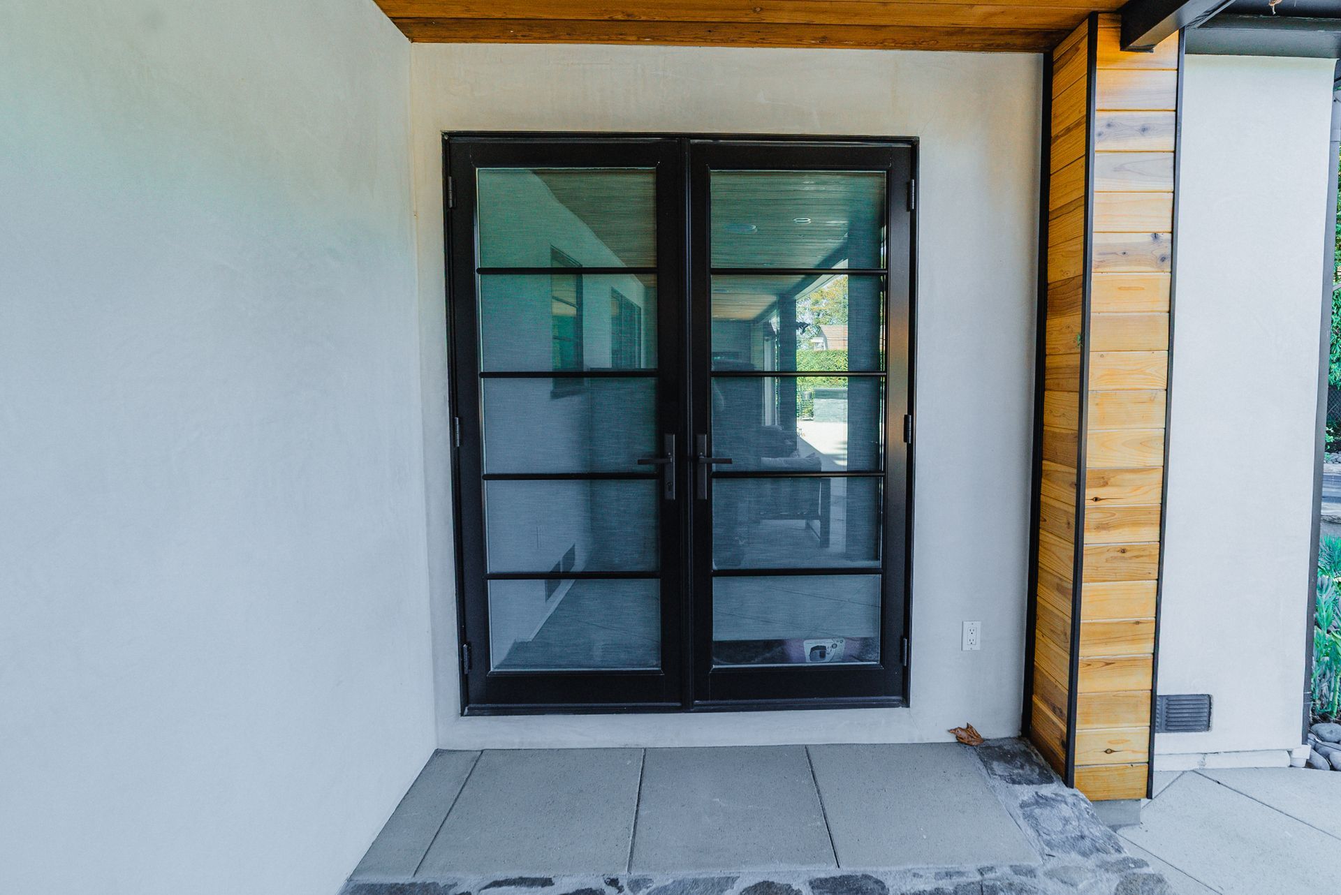 Black framed glass French doors on a white stucco wall. Wooden beam overhead, weathered wood pillar to the right.
