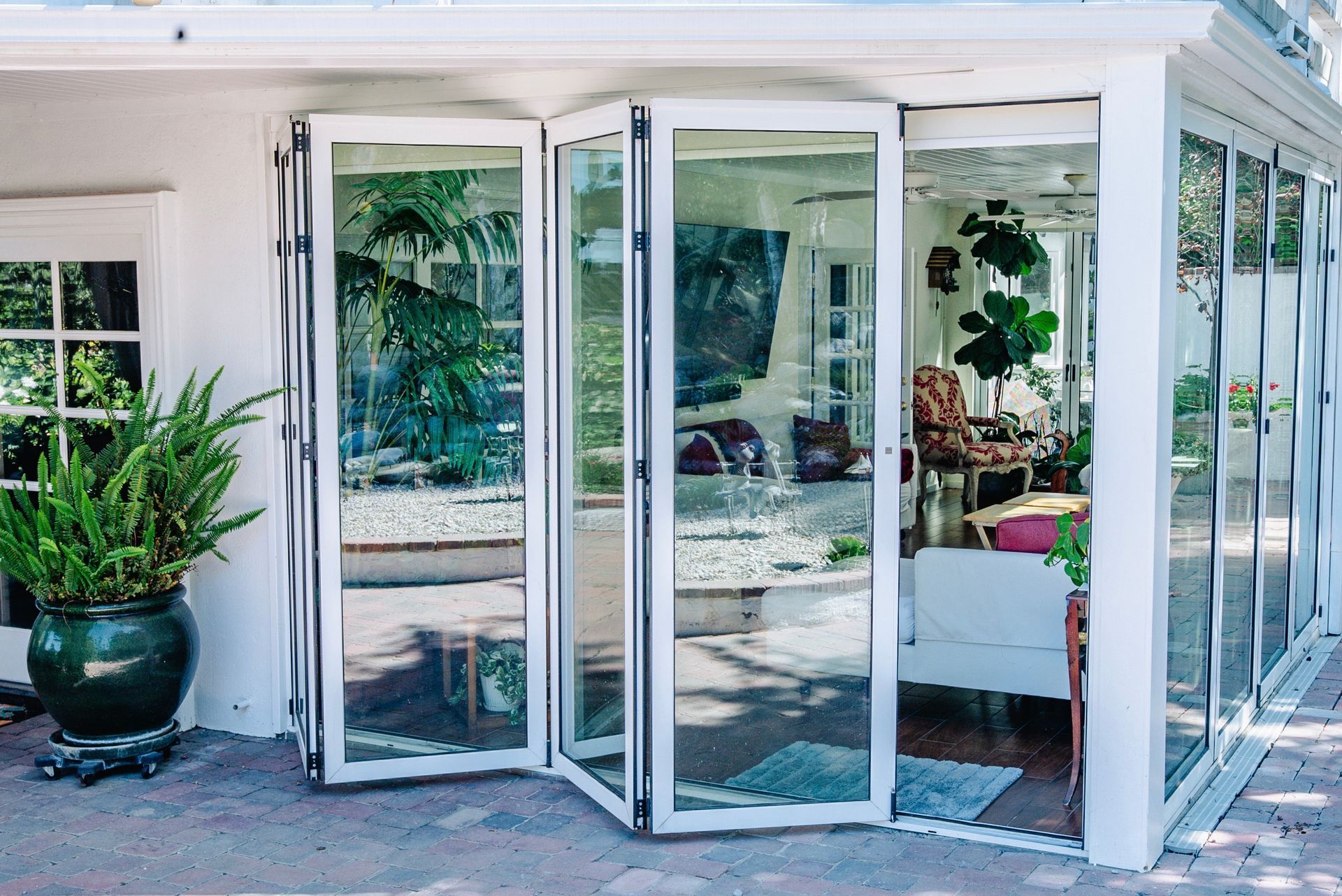 Folding glass doors on a building's exterior, surrounded by a patio and garden with flowers and rocks.