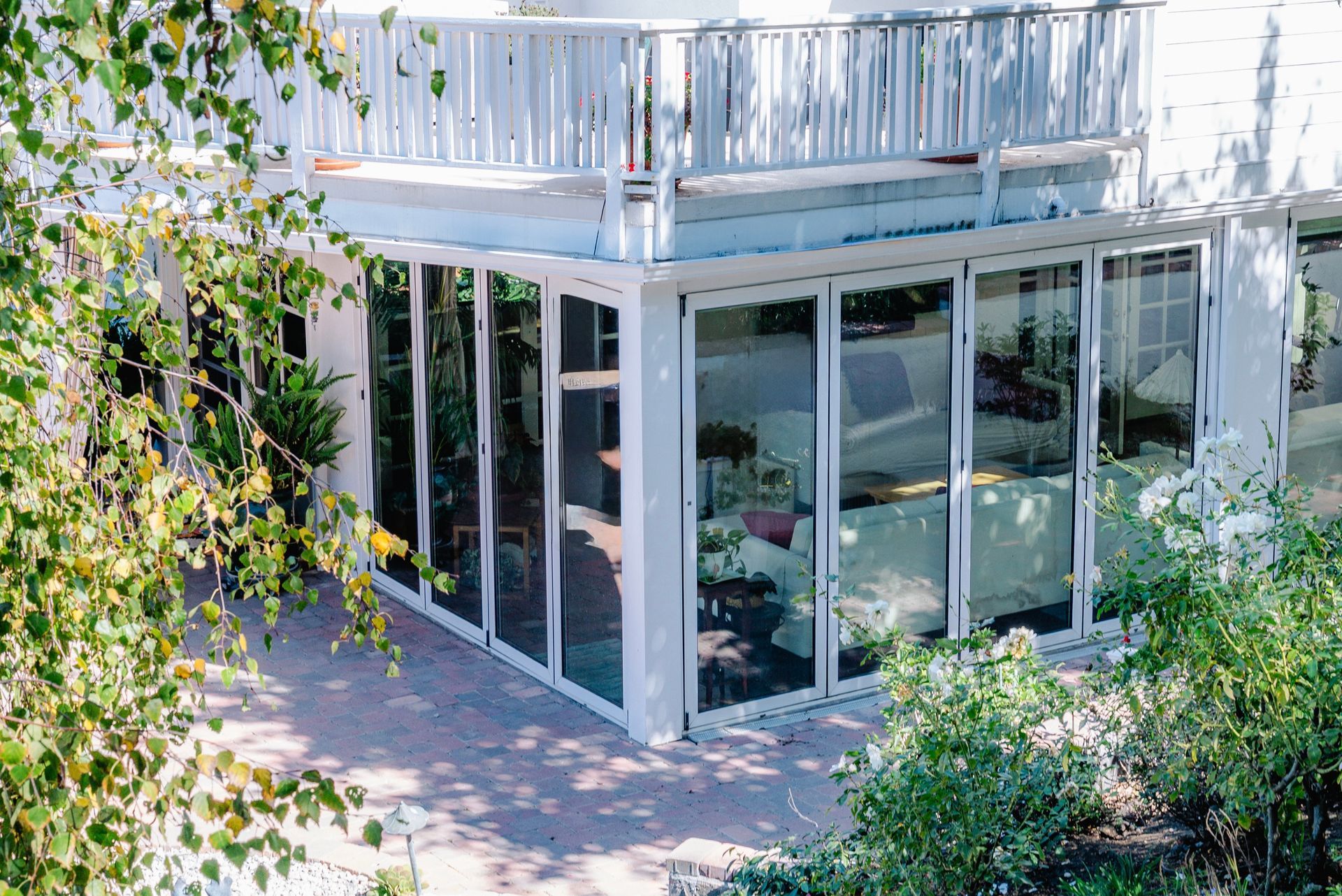 White building with glass sliding doors, balcony, and foliage.
