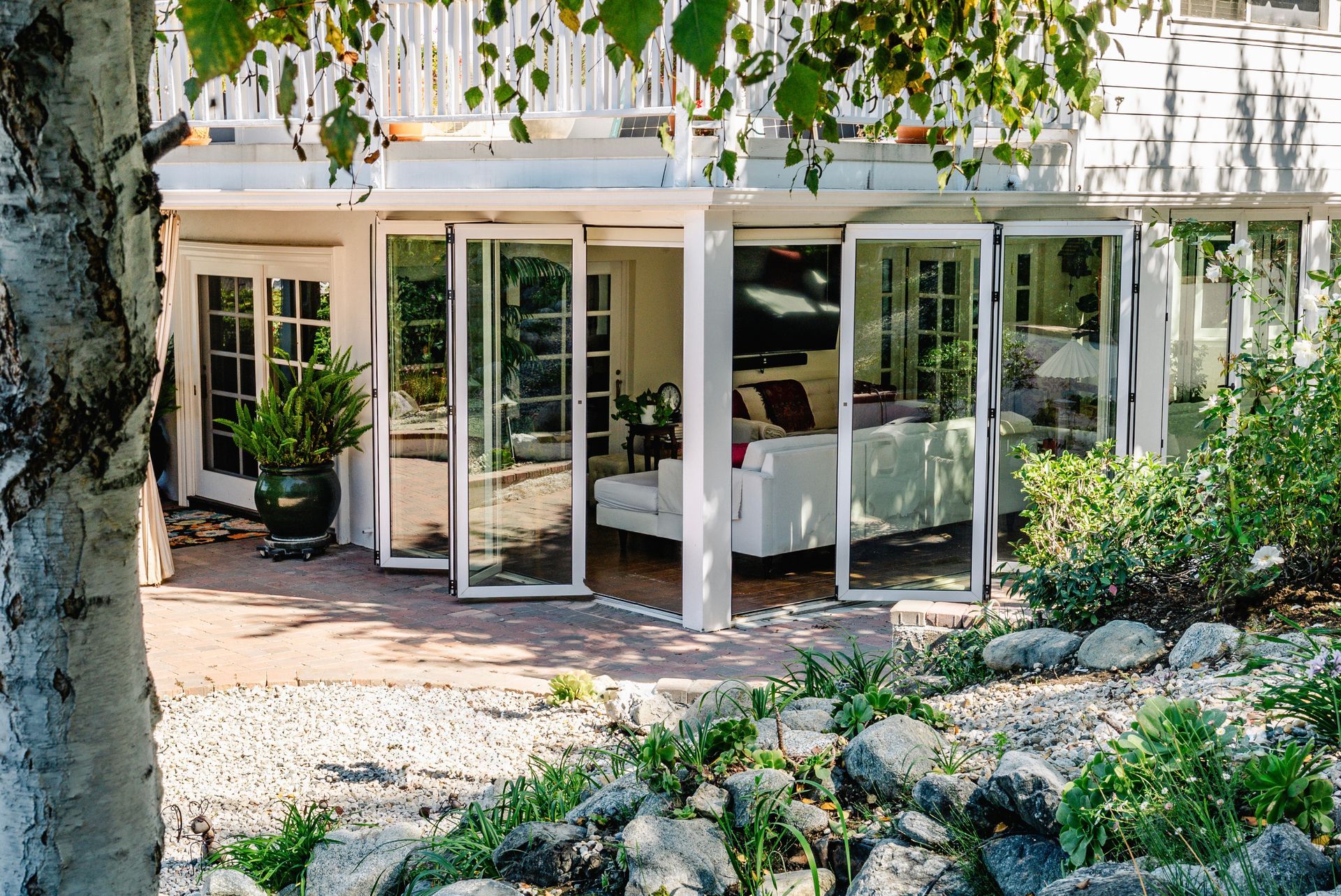 Patio with open folding glass doors, white furniture, and a garden.