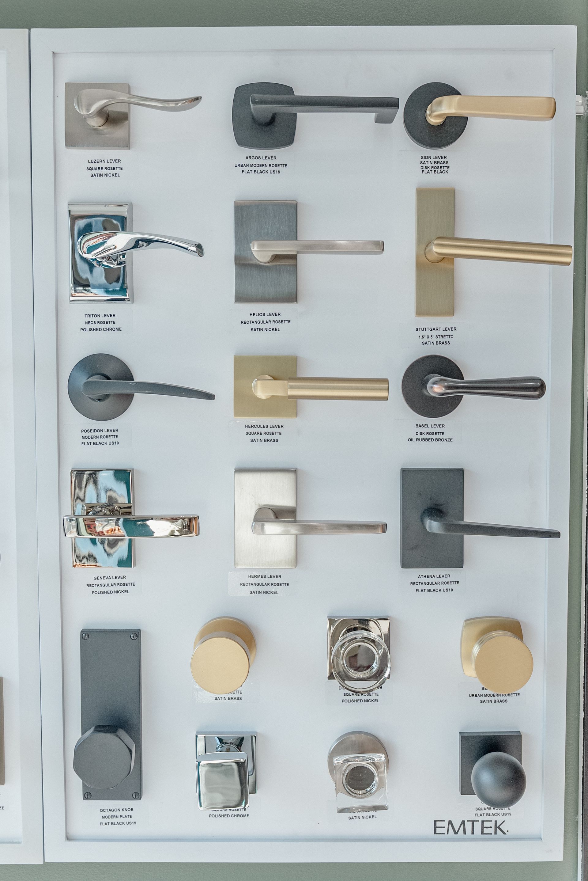 Display of various door handle styles on a white board; metal finishes in black, brass, and silver.
