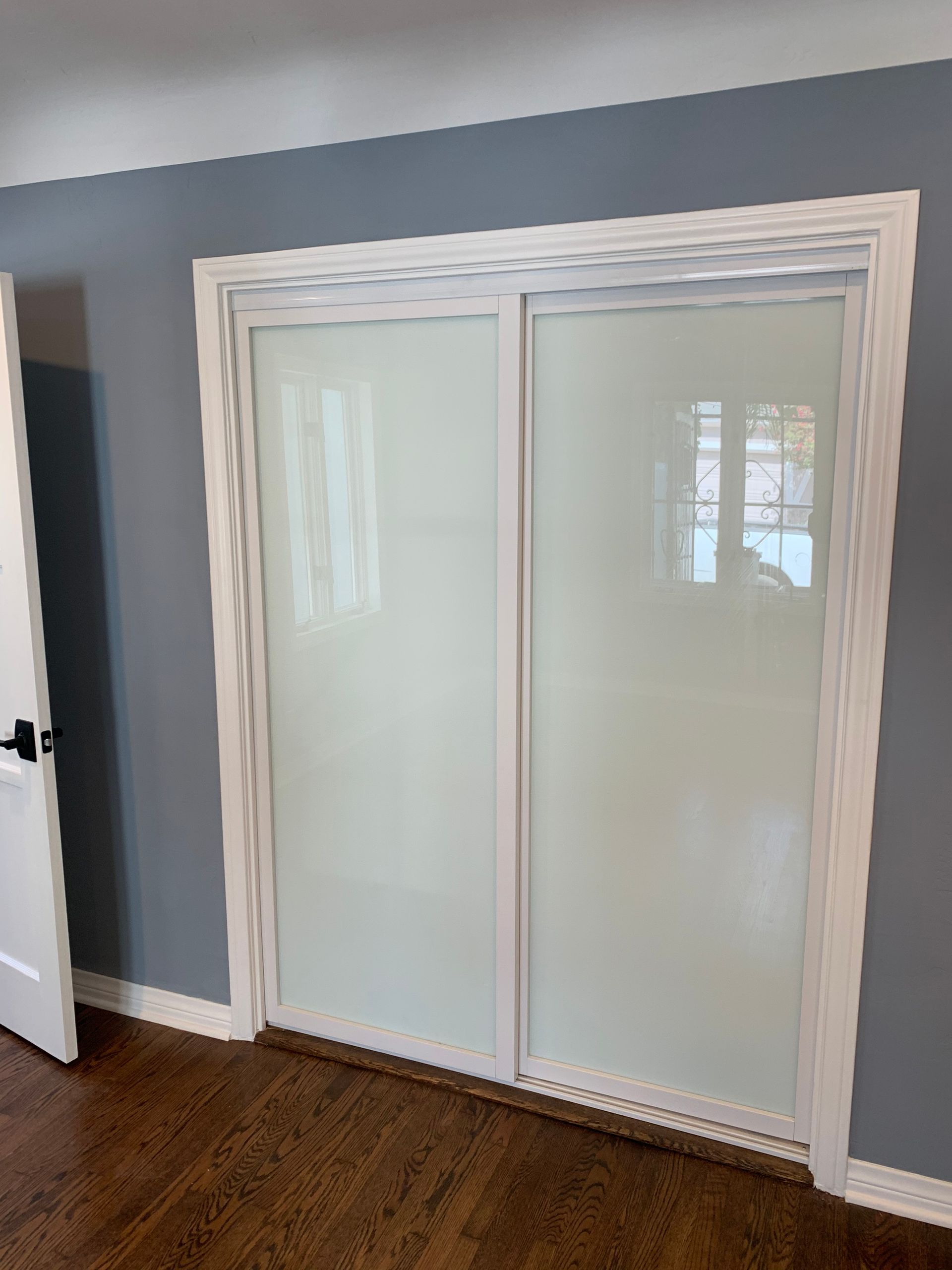 Sliding closet doors with frosted glass in a room with white trim, gray walls, and a dark wood floor.