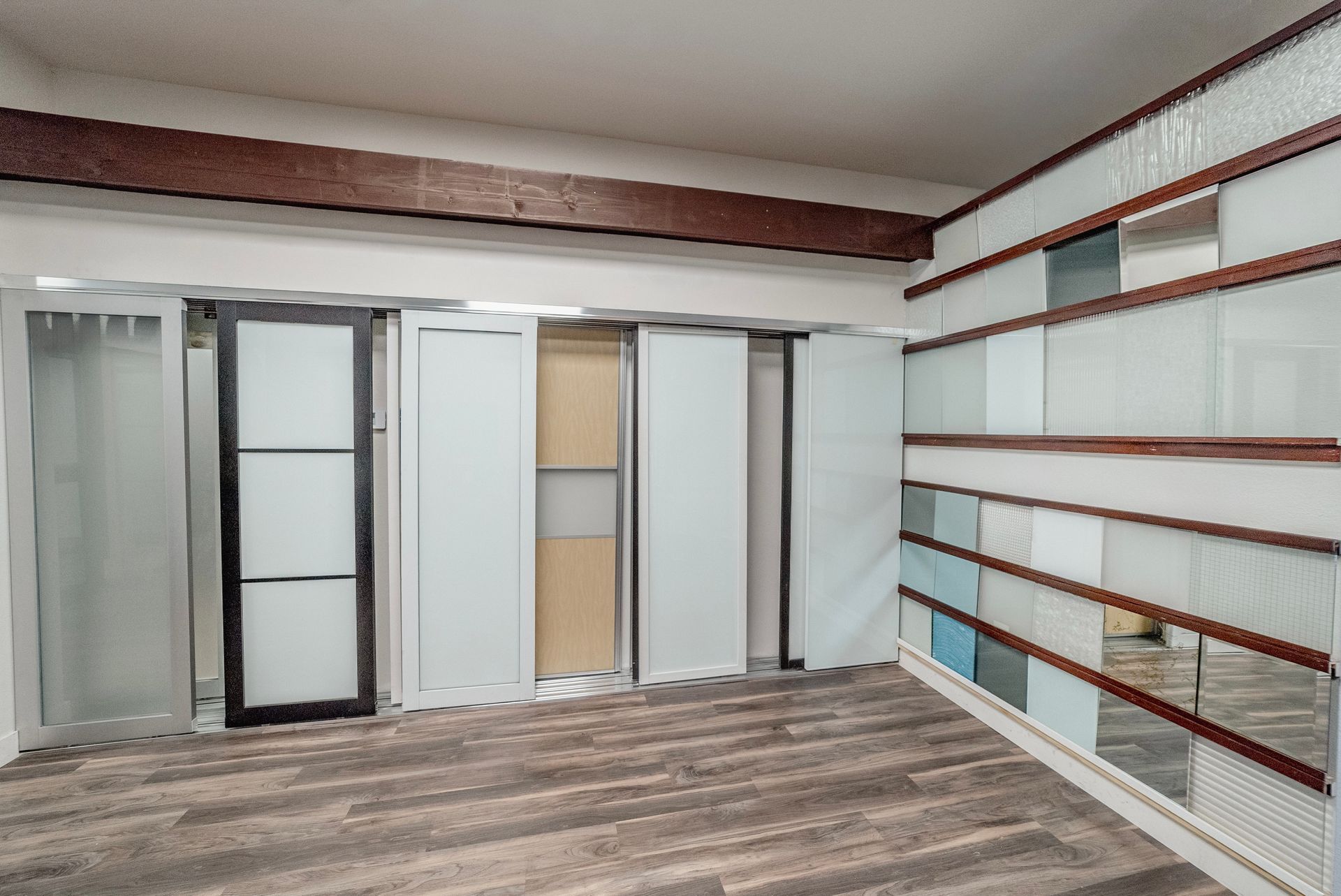 Room with various glass panels and a wood beam. The floor is wood-look laminate.