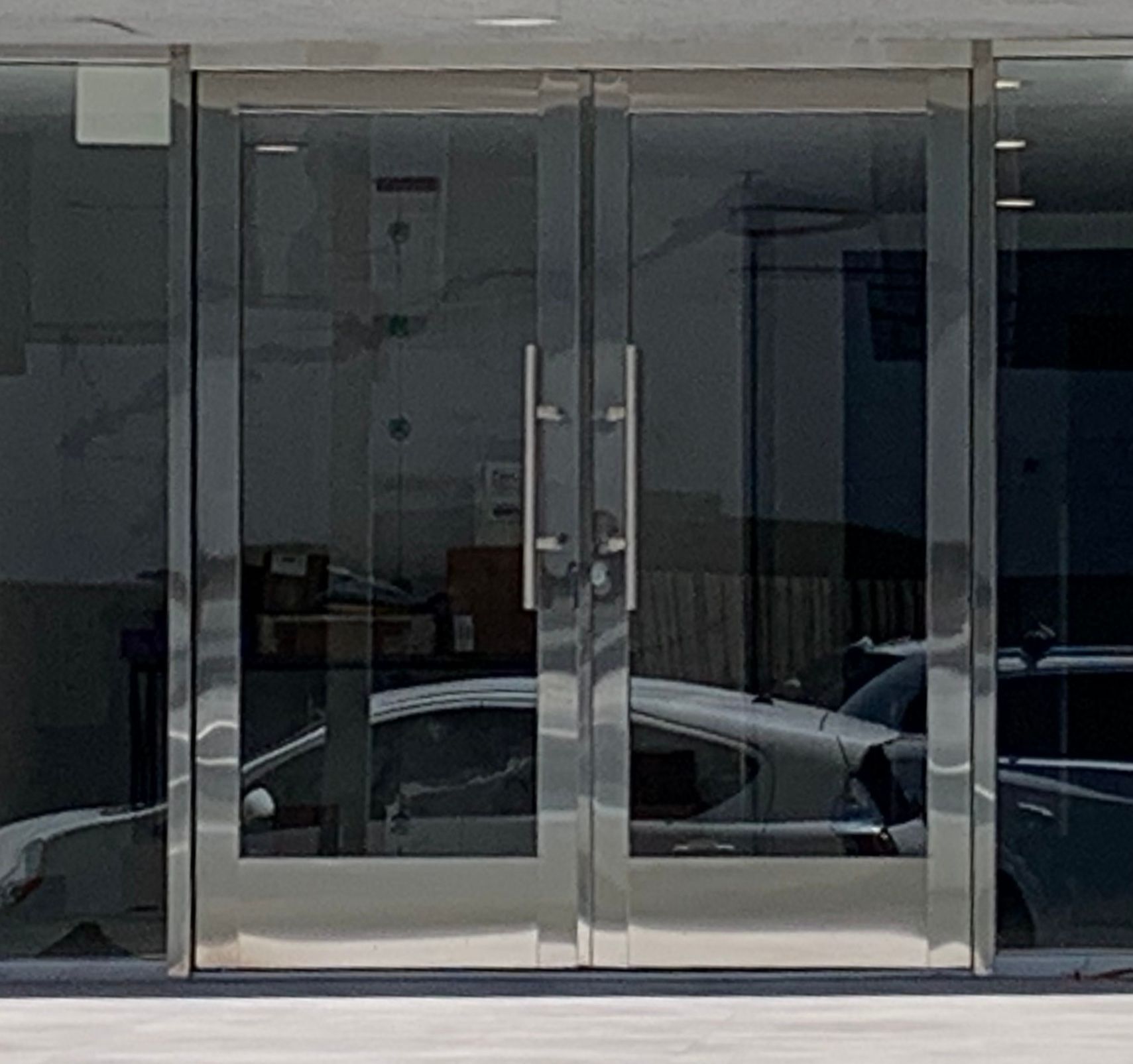 Glass double doors with stainless steel frames; a car is reflected in the glass.