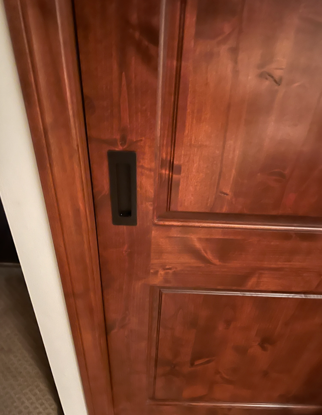 Close-up of a stained wooden door with a black recessed pull.