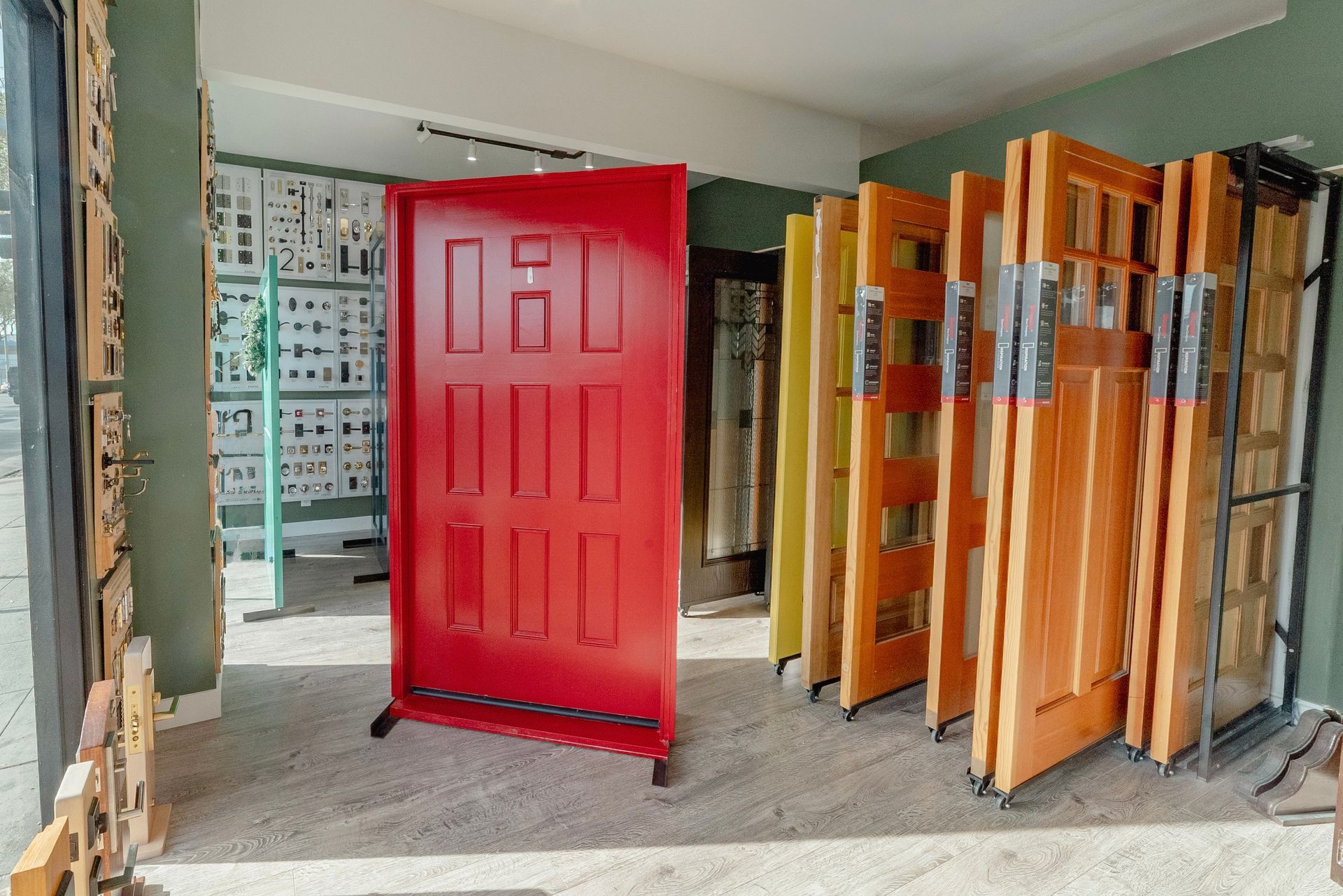 Red door on display in a store, surrounded by other wooden doors of varying styles and colors.
