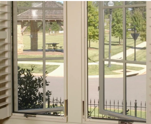Two open windows with screens, overlooking a park with a pavilion and trees.
