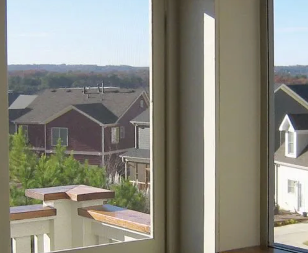 View of houses and trees from a window, with a railing in the foreground. Sunny day.