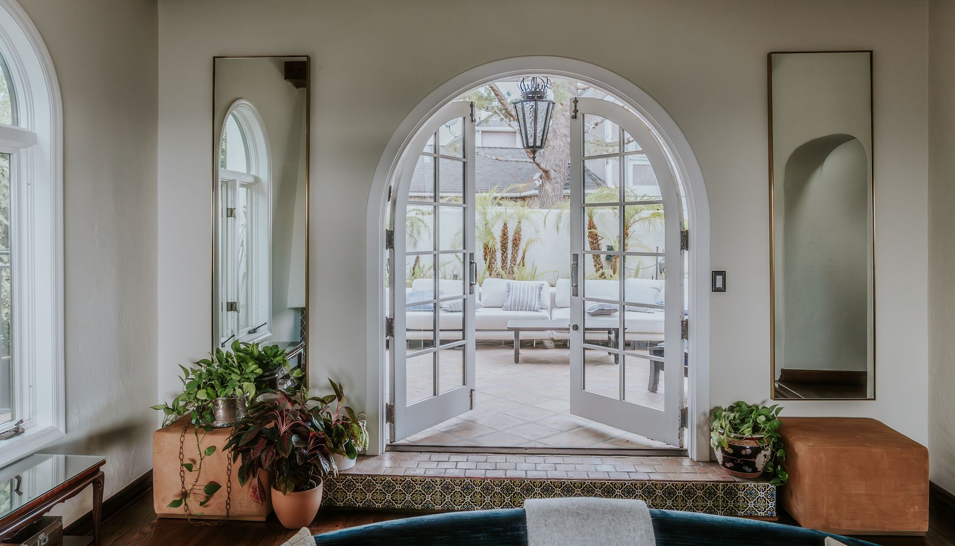 Bright white entryway with arched French doors, mirrors, plants, and a tiled floor leading outside