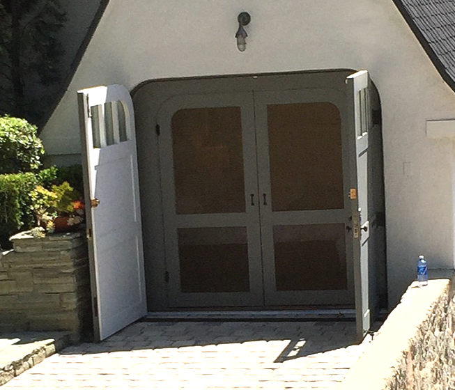 White double doors at the entrance of a house, with one side door open and sunlight on the walkway.