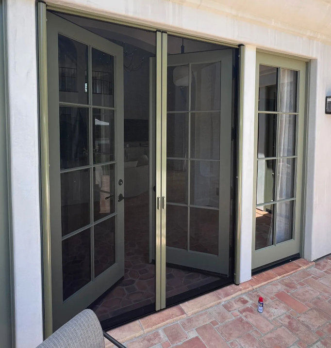 Retractable screen doors installed on a multi-panel patio door set with light green frames and a brick patio floor.