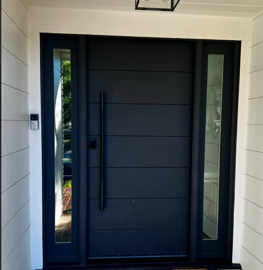 Dark gray front door with a long handle, flanked by glass side panels.