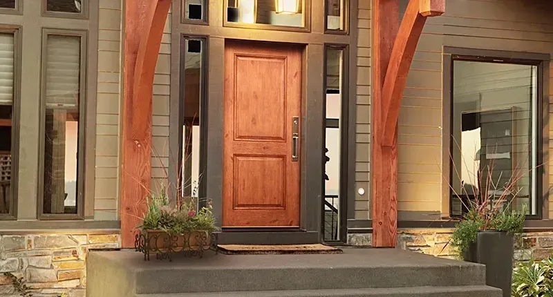 Glass entry door revealing wooden staircase. Exterior with light gray stucco and brown wood siding.