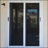 Sliding screen door with white frame, black screen. Outdoors, house in background.