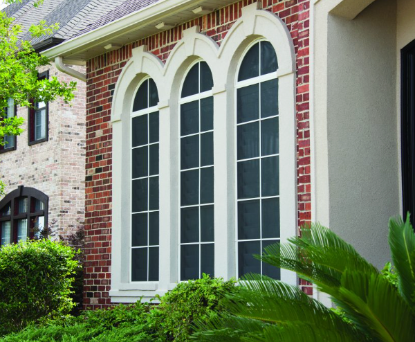Three tall arched windows with white trim on a brick house.