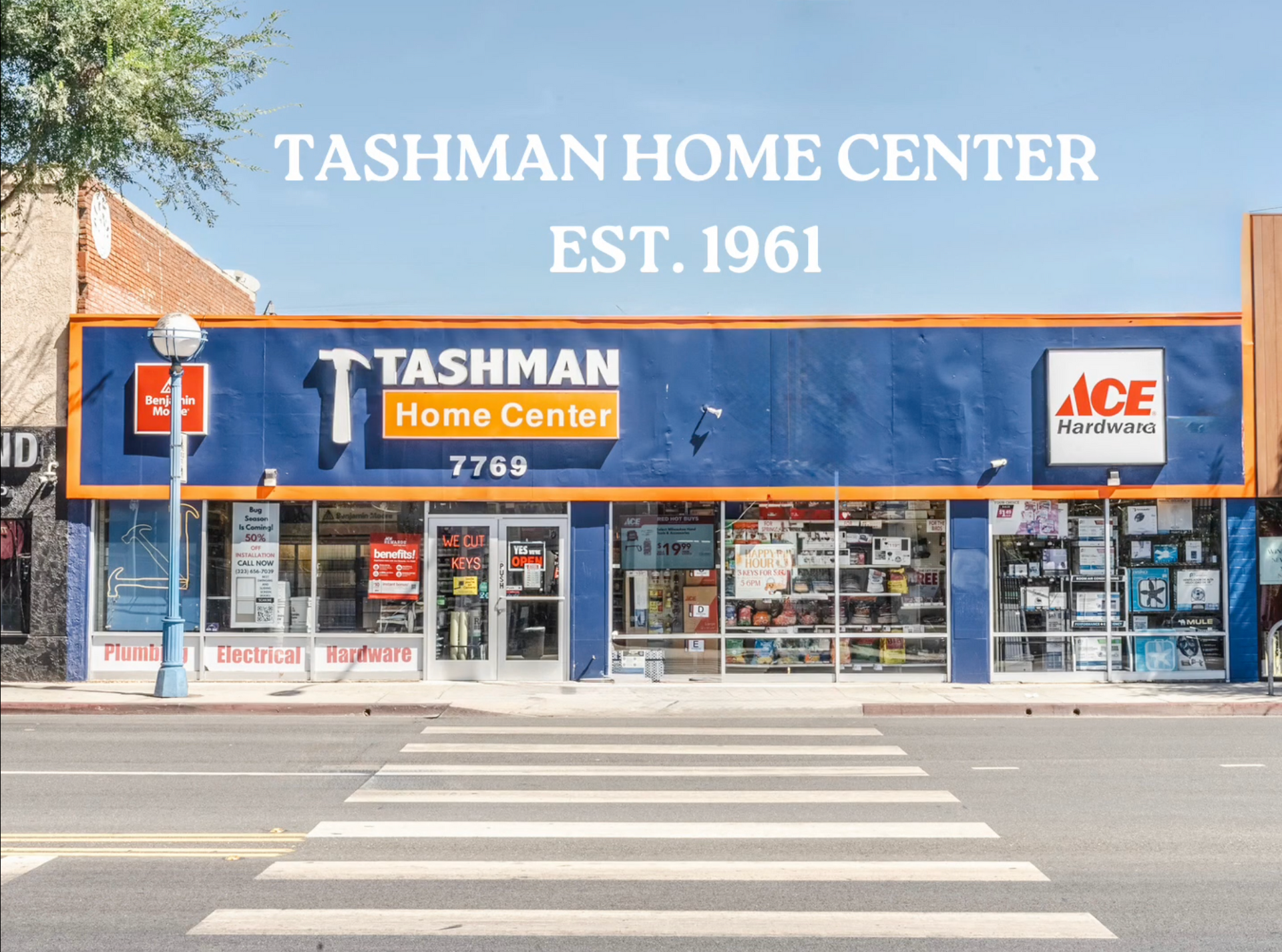 Tashman Home Center store with blue exterior, Ace Hardware sign, and crosswalk. Est. 1961.
