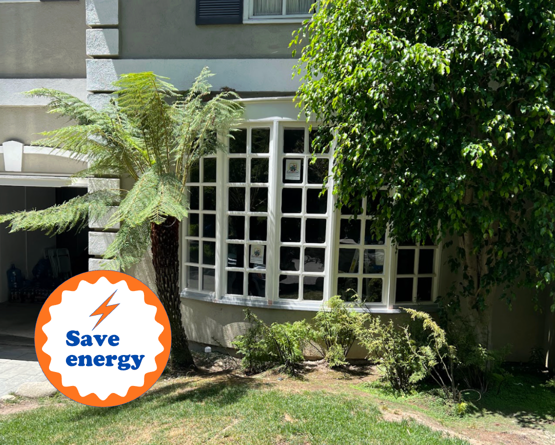 Window of a house, with energy-saving text, surrounded by greenery and lawn.