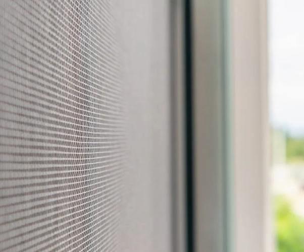 Close-up of a window screen; gray mesh, vertical lines, frame edge visible.