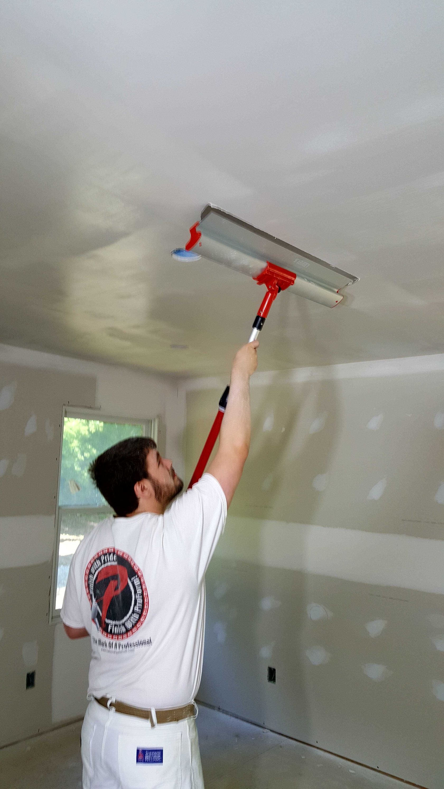A man is painting the ceiling of a room with a trowel.