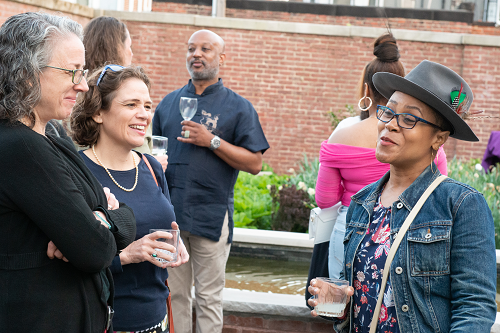 A group of people are standing in front of a brick wall talking to each other.