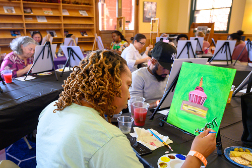 A woman is painting a picture of a cake on a canvas.