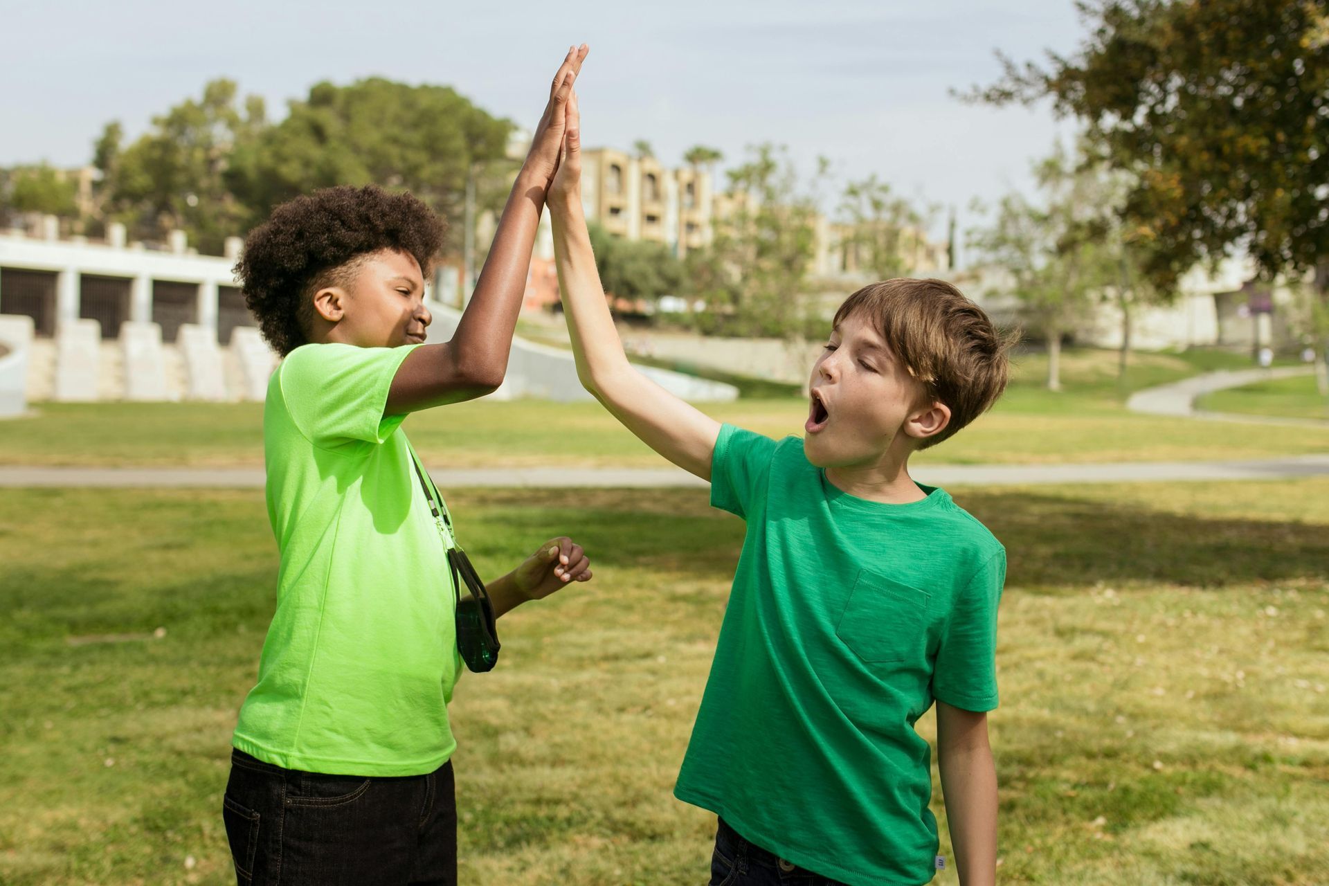 Two young boys are giving each other a high five in a park.