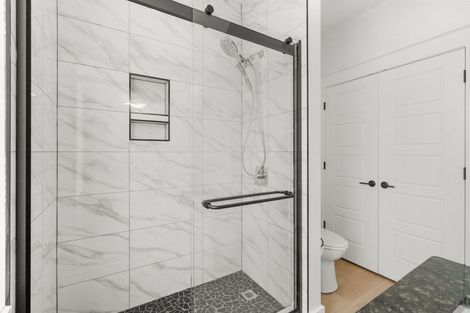 Modern bathroom with marble shower, glass door, and white double doors beside a toilet