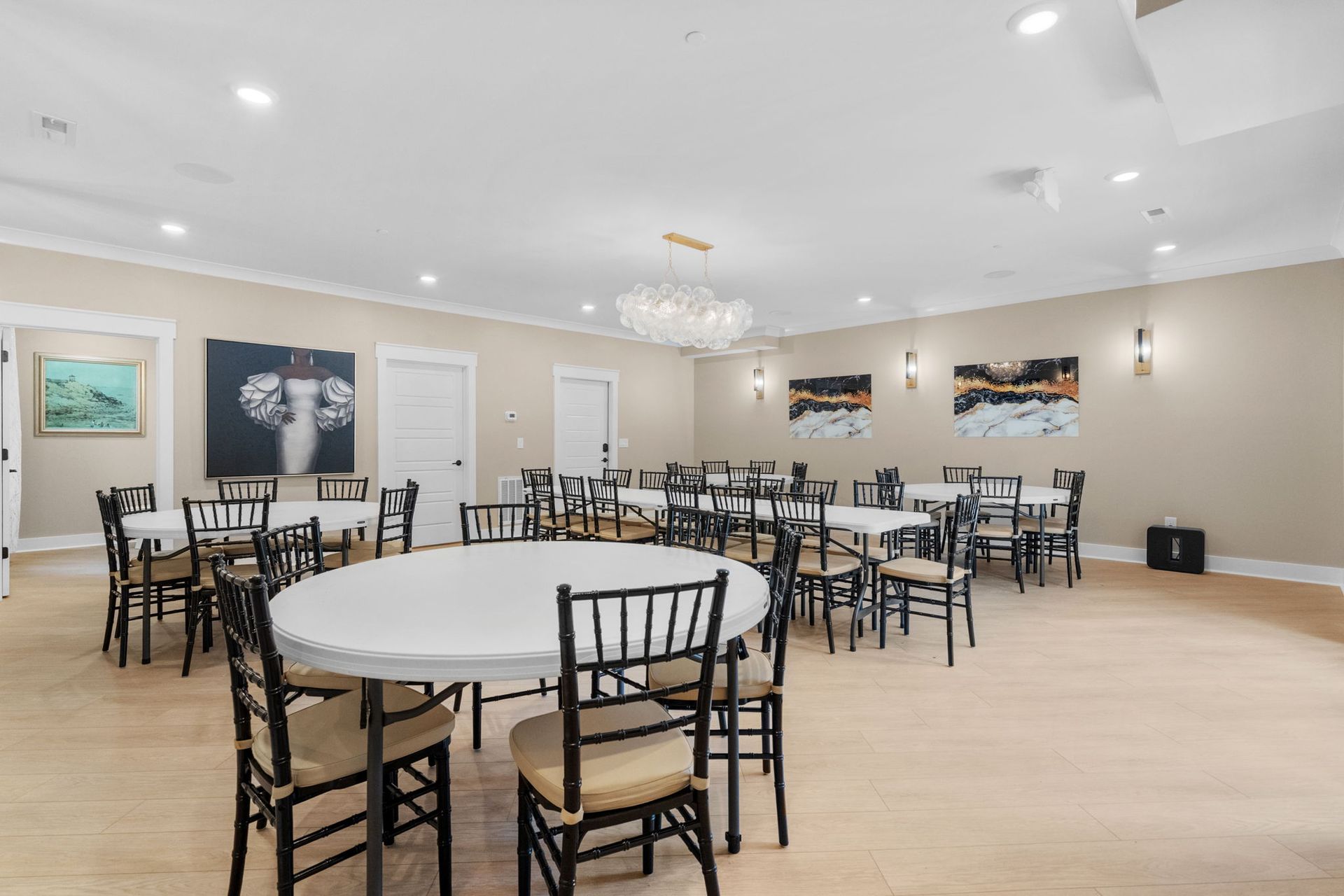 Empty banquet hall with round tables, black chairs, white ceiling, and wall art under bright lighting