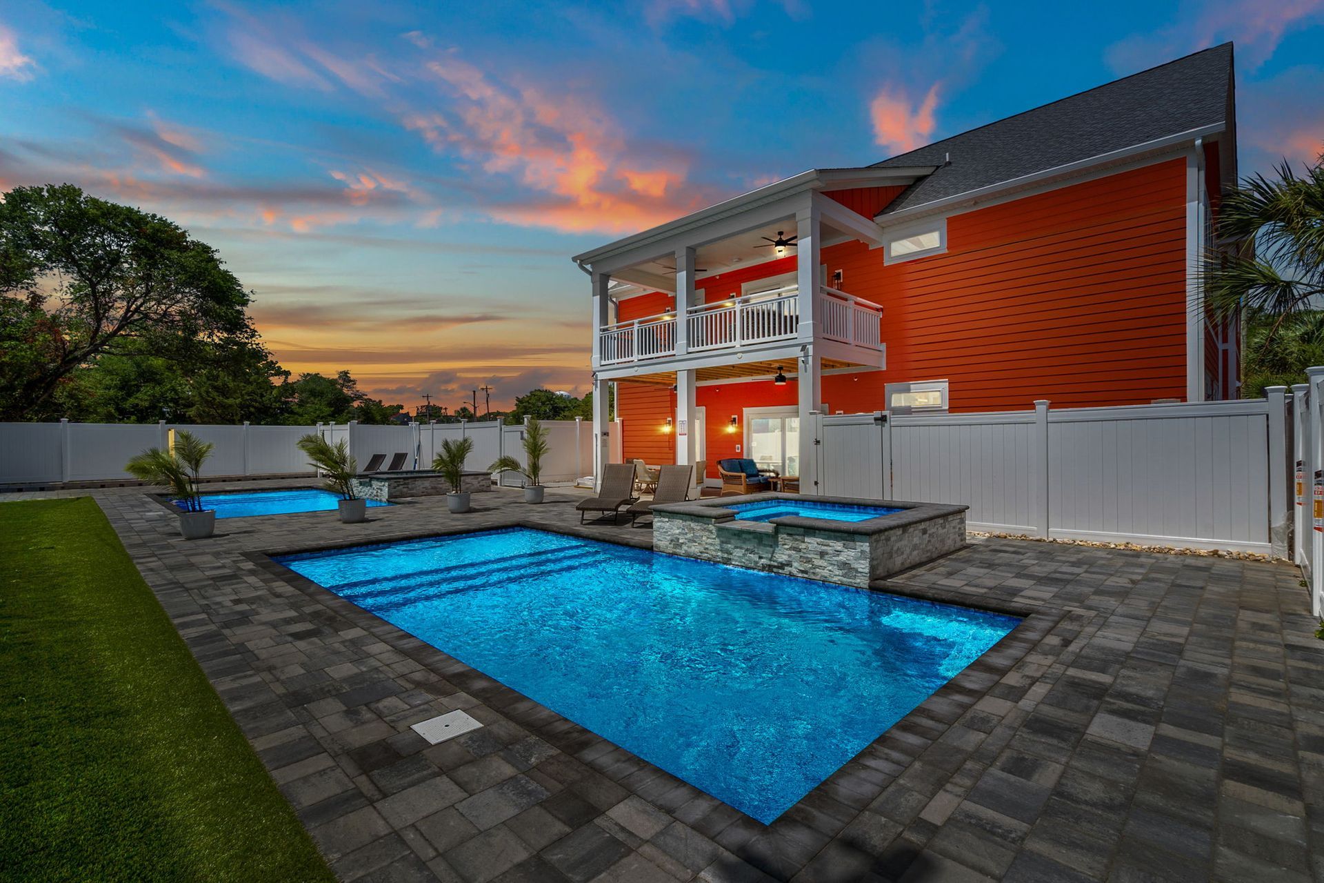 Modern two-story house with lit pool and patio at sunset