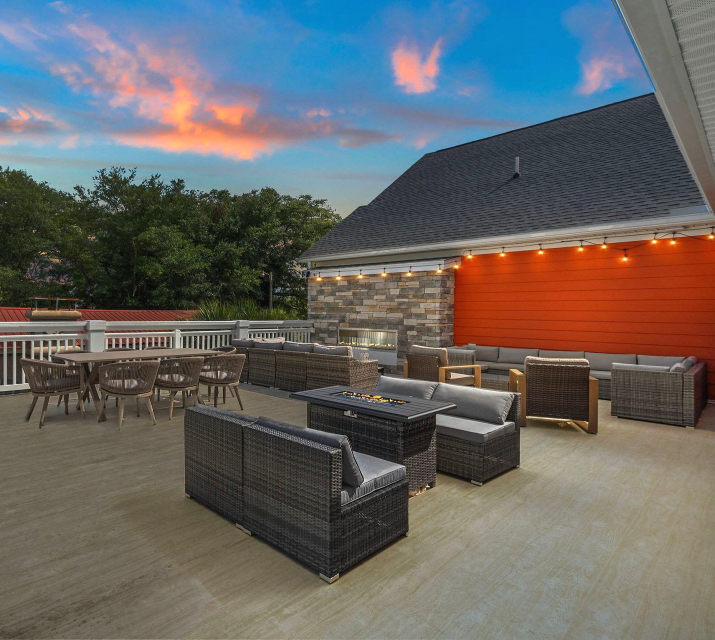Outdoor patio with wicker seating, dining tables, and a stone fire feature at dusk