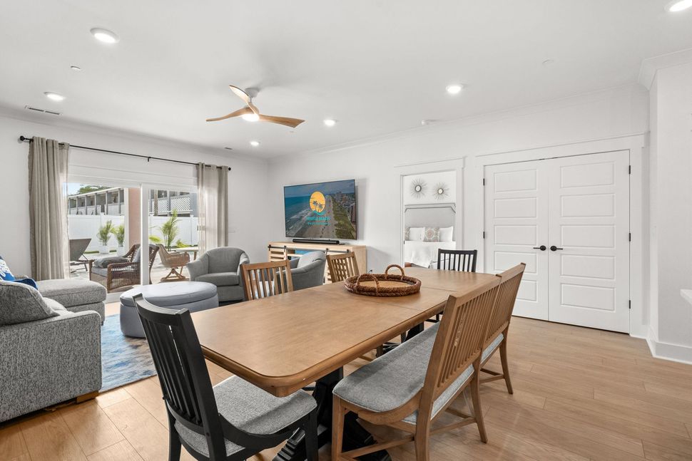 Bright open living-dining room with wooden table, gray sofa, sliding glass doors, and white built-in cabinets