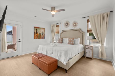 Bright white bedroom with a bed, tufted bench, ceiling fan, and gold sunburst wall decor