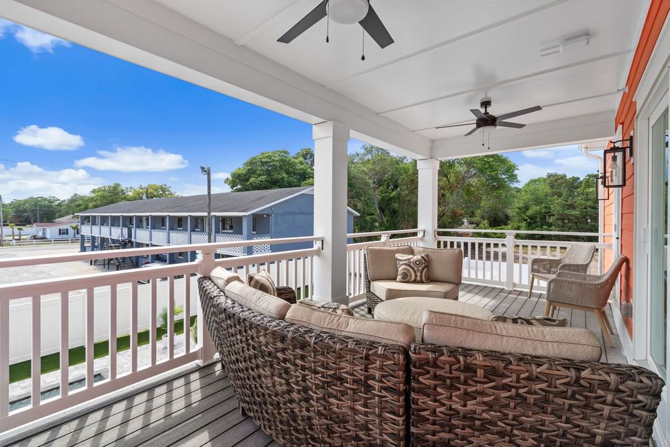 Covered porch with wicker seating overlooking a pool and apartment buildings under a bright blue sky