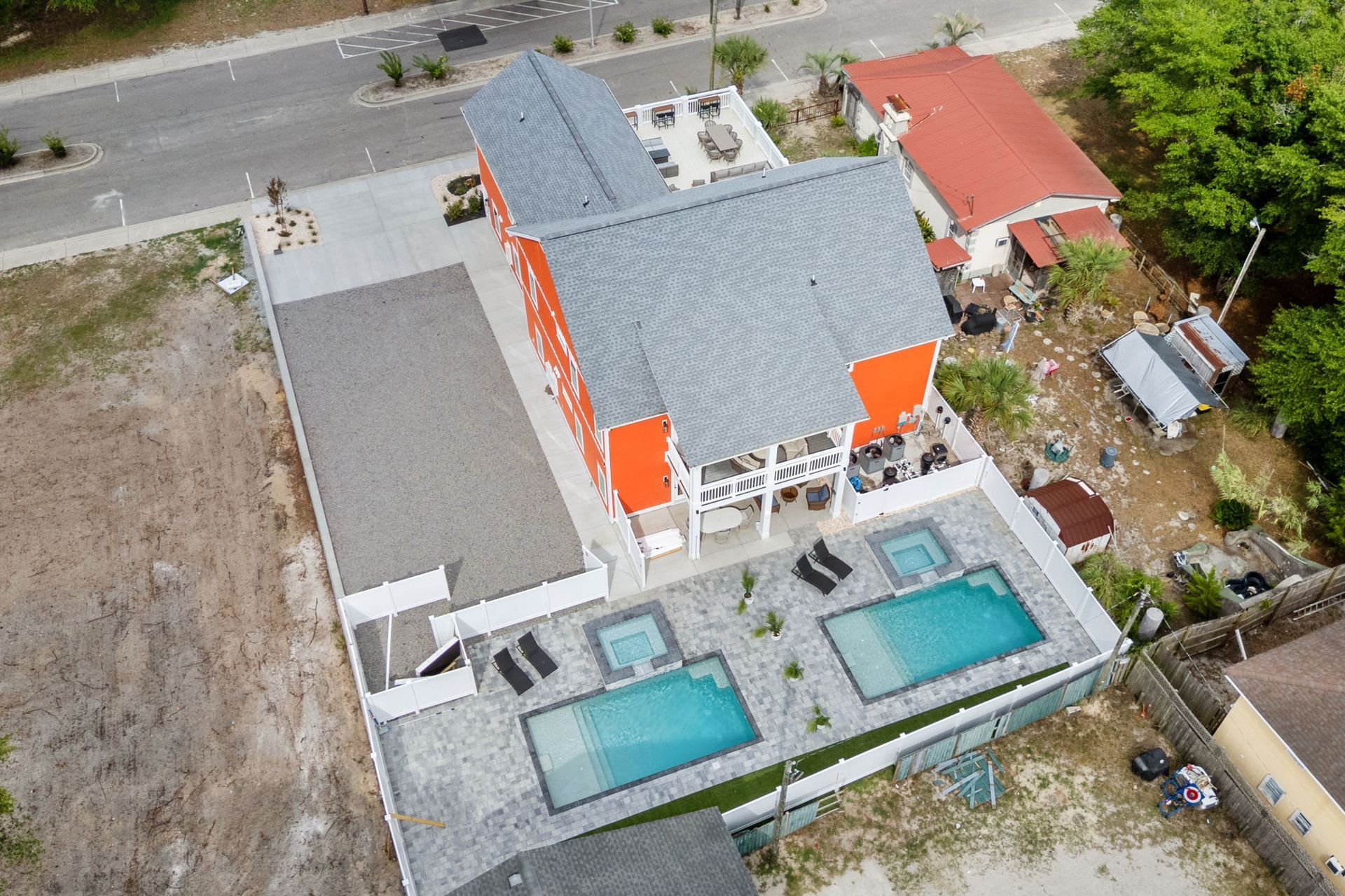Aerial view of a house with a gray roof, white balcony, and two turquoise pools beside a road.