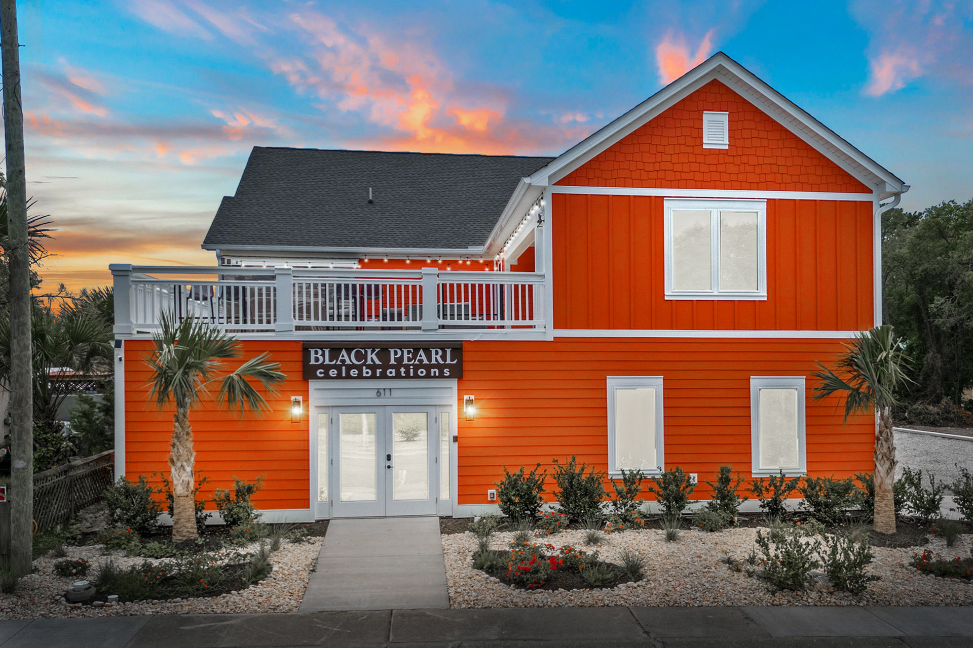 Orange two-story building at sunset with a balcony and sign reading “Black Pearl Celebrations.”