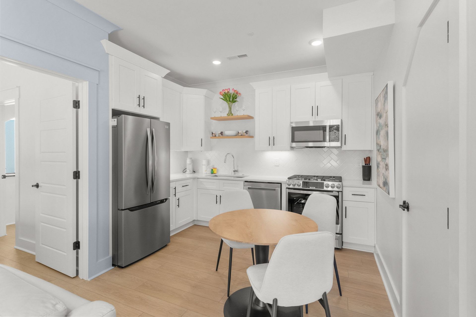 Bright modern white kitchen with stainless appliances and a small round dining table