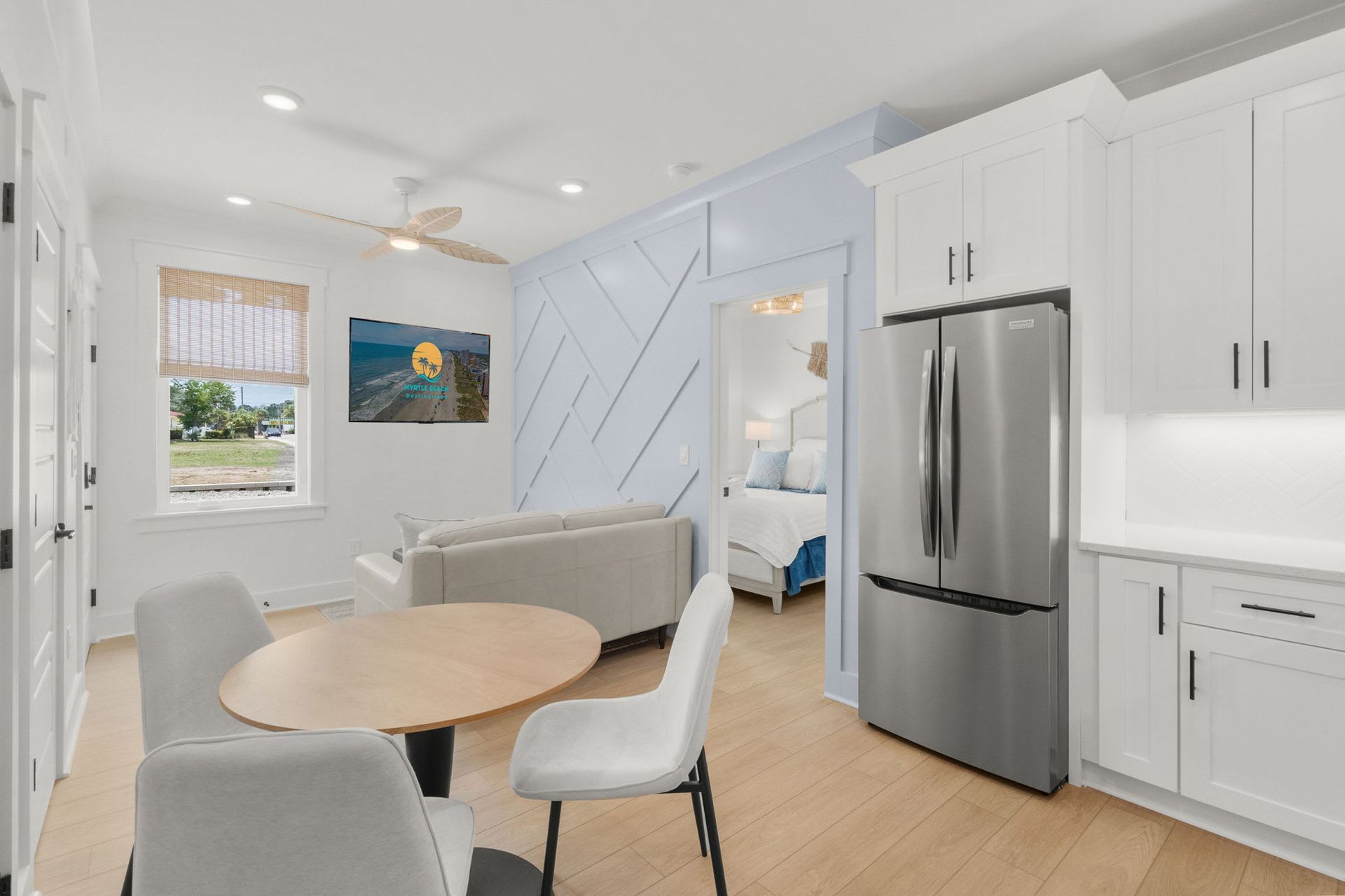 Bright modern kitchen with round table, white chairs, stainless steel fridge, and light blue accents