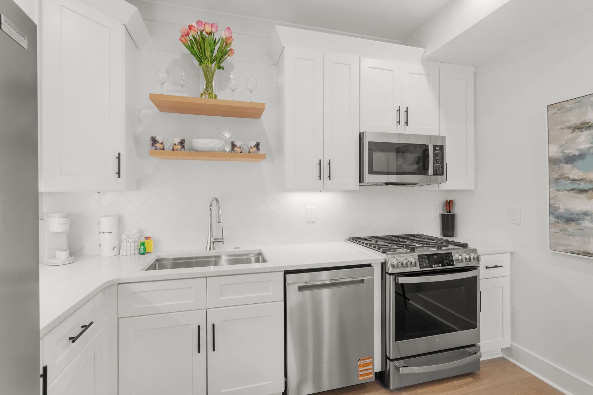 Bright white kitchen with stainless steel appliances, open shelves, and a small vase of flowers.