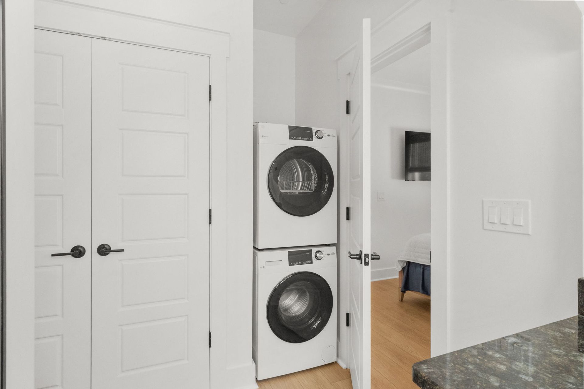 White laundry closet with stacked washer and dryer beside an open doorway in a bright home interior