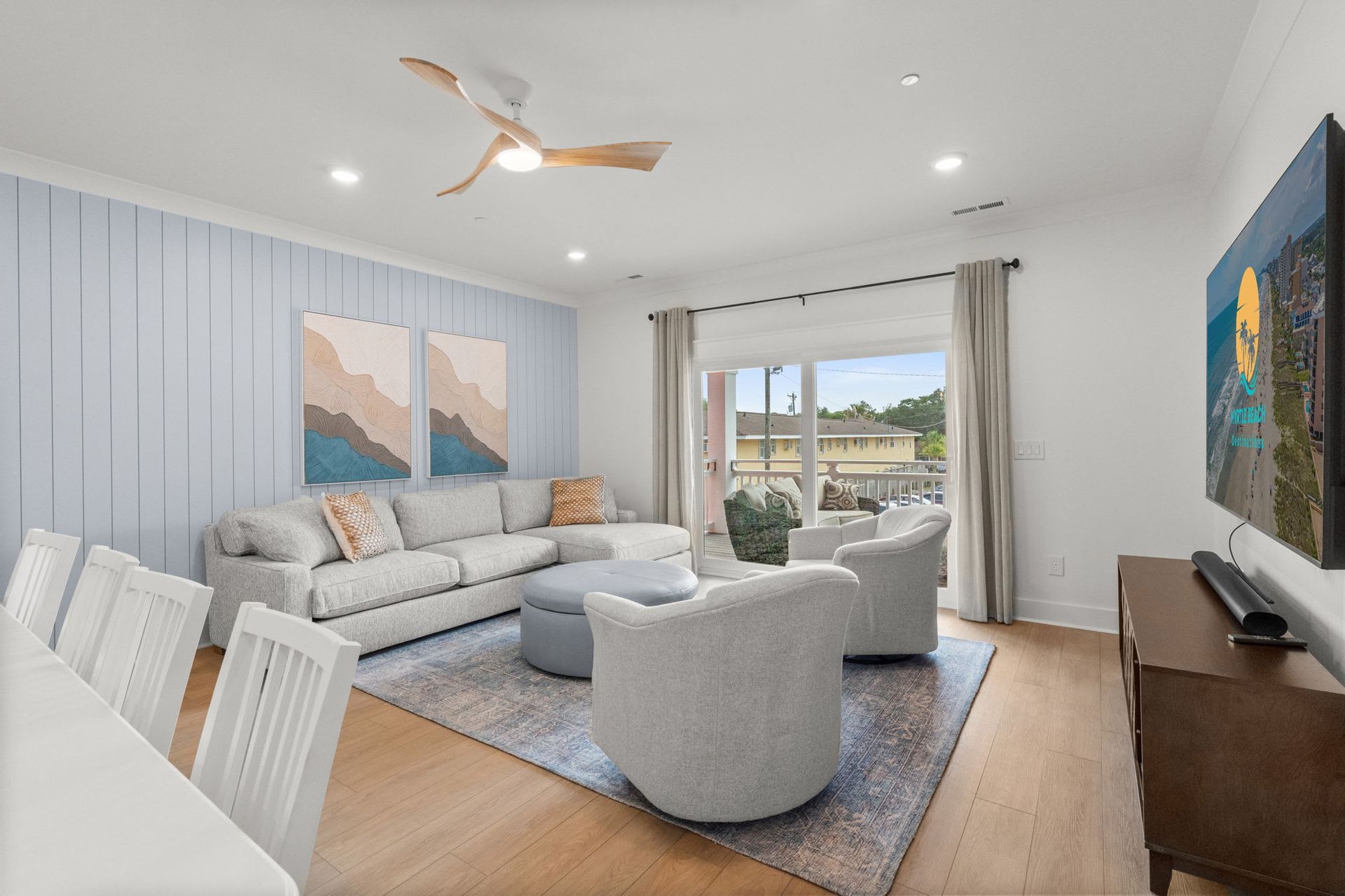 Bright living room with gray sectional, two armchairs, wall art, TV, and sliding doors to a balcony.