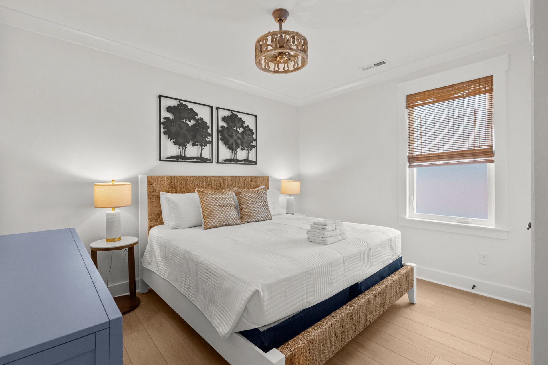 Bright bedroom with white bedding, wood furniture, and framed wall art near a window
