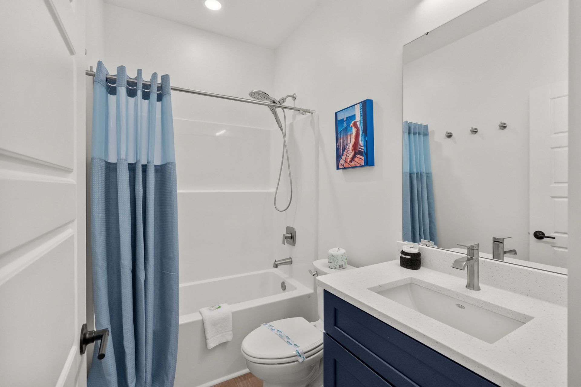 Bright white bathroom with blue shower curtain, toilet, vanity, and wall-mounted showerhead