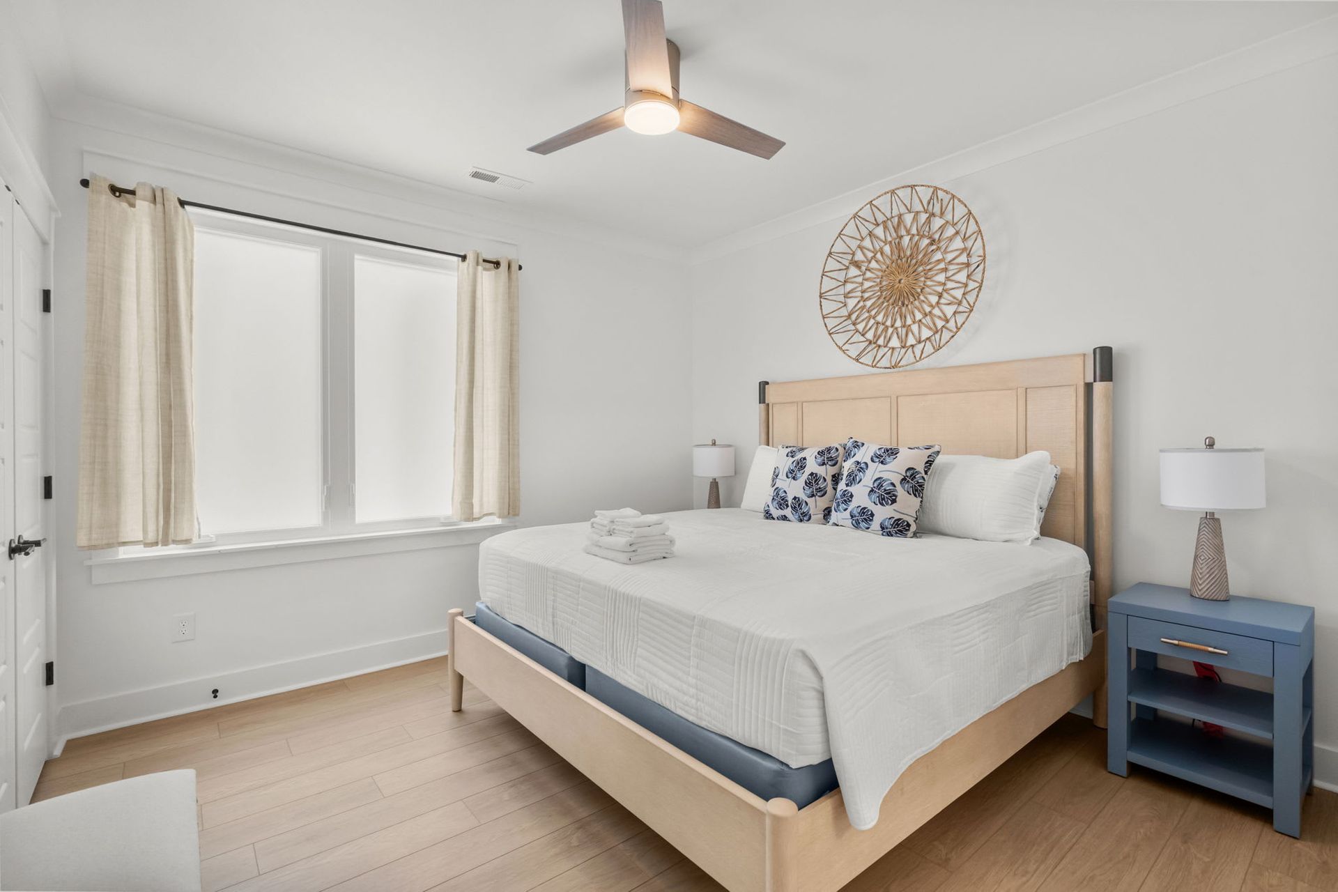 Bright bedroom with a bed, blue nightstand, window, and ceiling fan in a minimalist design