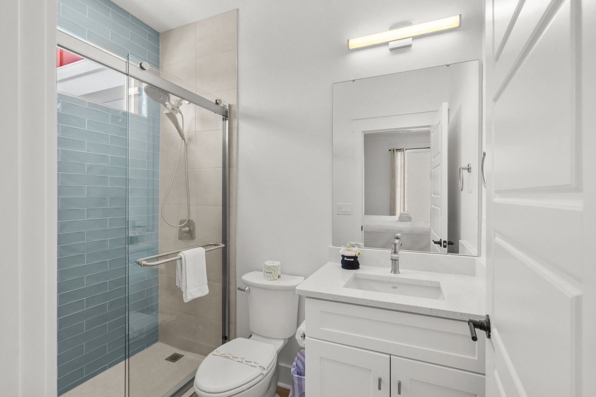 Bright bathroom with glass shower, white vanity, toilet, and large mirror