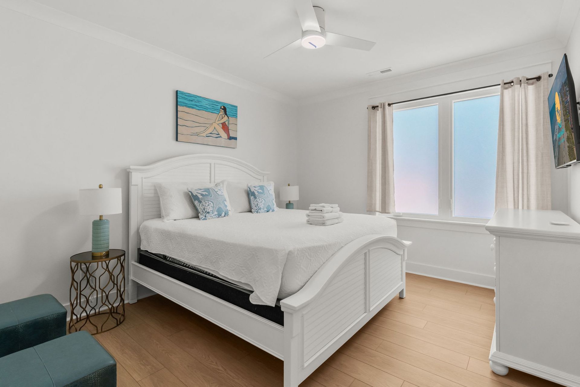 Bright bedroom with white bed, teal chair, window seat, and light wood floor
