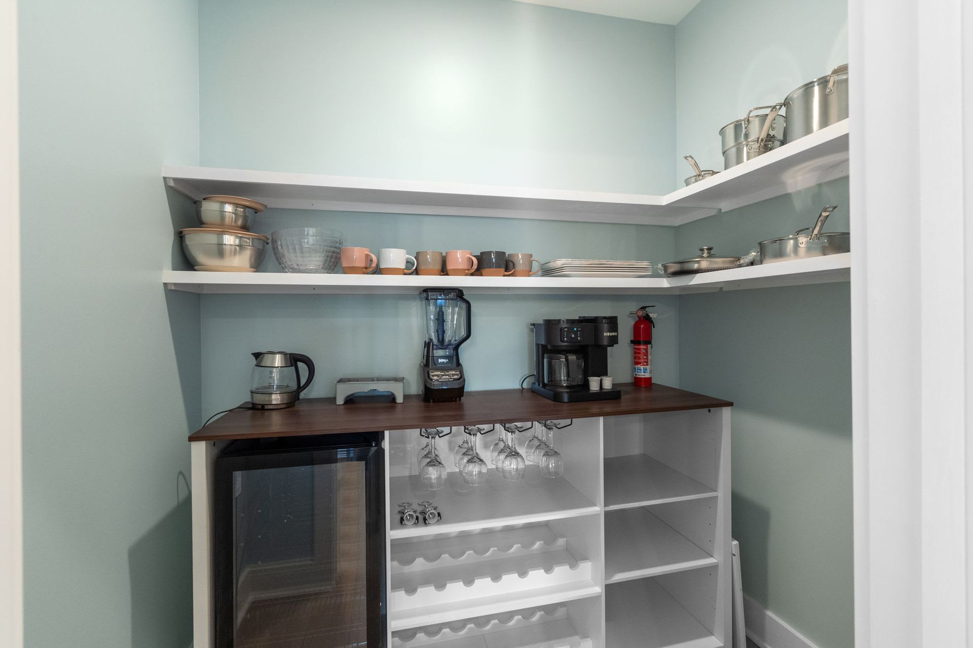 Small pantry with shelves, countertop coffee makers, mini fridge, and a glass-front cabinet