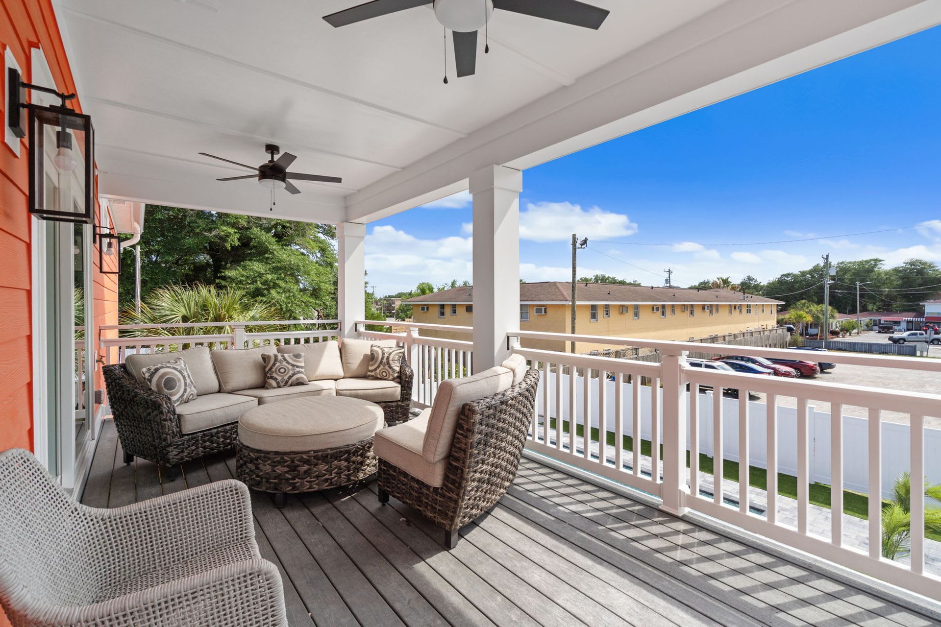Covered porch with wicker seating, white railing, ceiling fans, and a street view on a sunny day