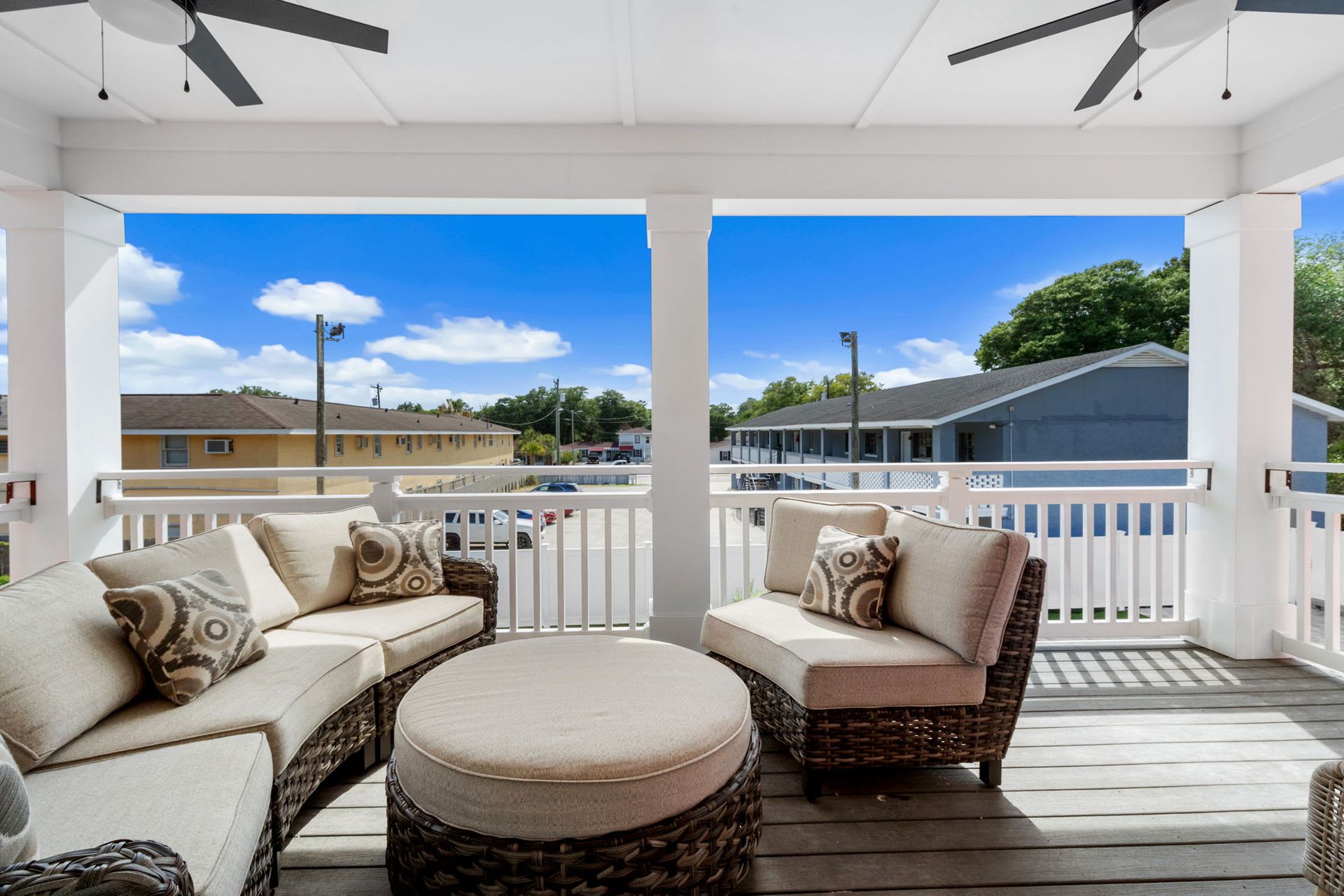 Porch with wicker seating and round ottoman overlooking a sunny neighborhood street.